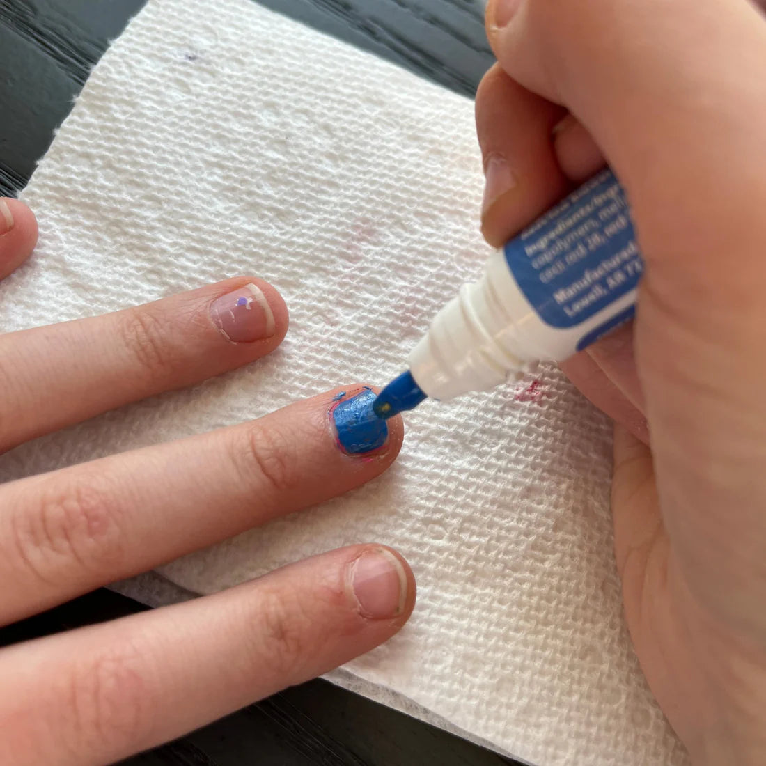 Child's hand being painted with Piggy Paint pen polishes in vibrant blue on a napkin