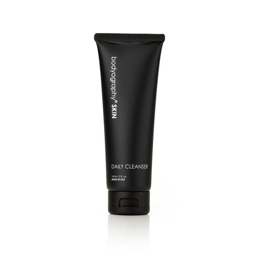 A black tube of Bodyography Skin Care Daily Cleanser 5 oz, featuring glycolic acid and free from sulfates and parabens, stands upright on a white background. The label lists product details and its 5 oz (140 ml) volume.