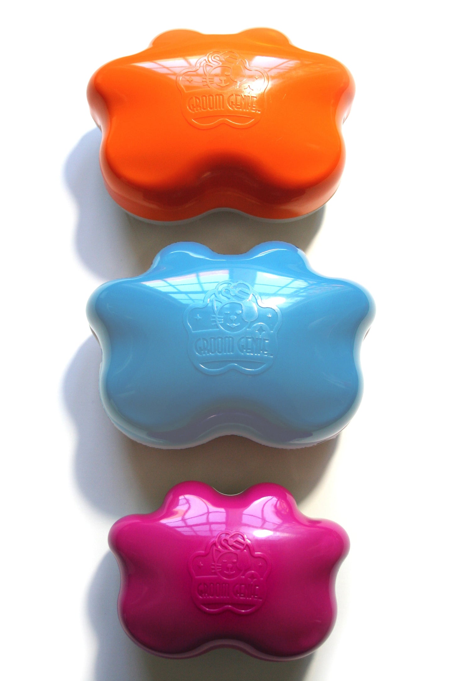Three paw-shaped plastic containers, stacked vertically—orange on top, light blue in the middle, pink at the bottom—are ideal for storing Groom Genie Original Pet Detangling Brush and each lid displays an embossed Crown Center logo.