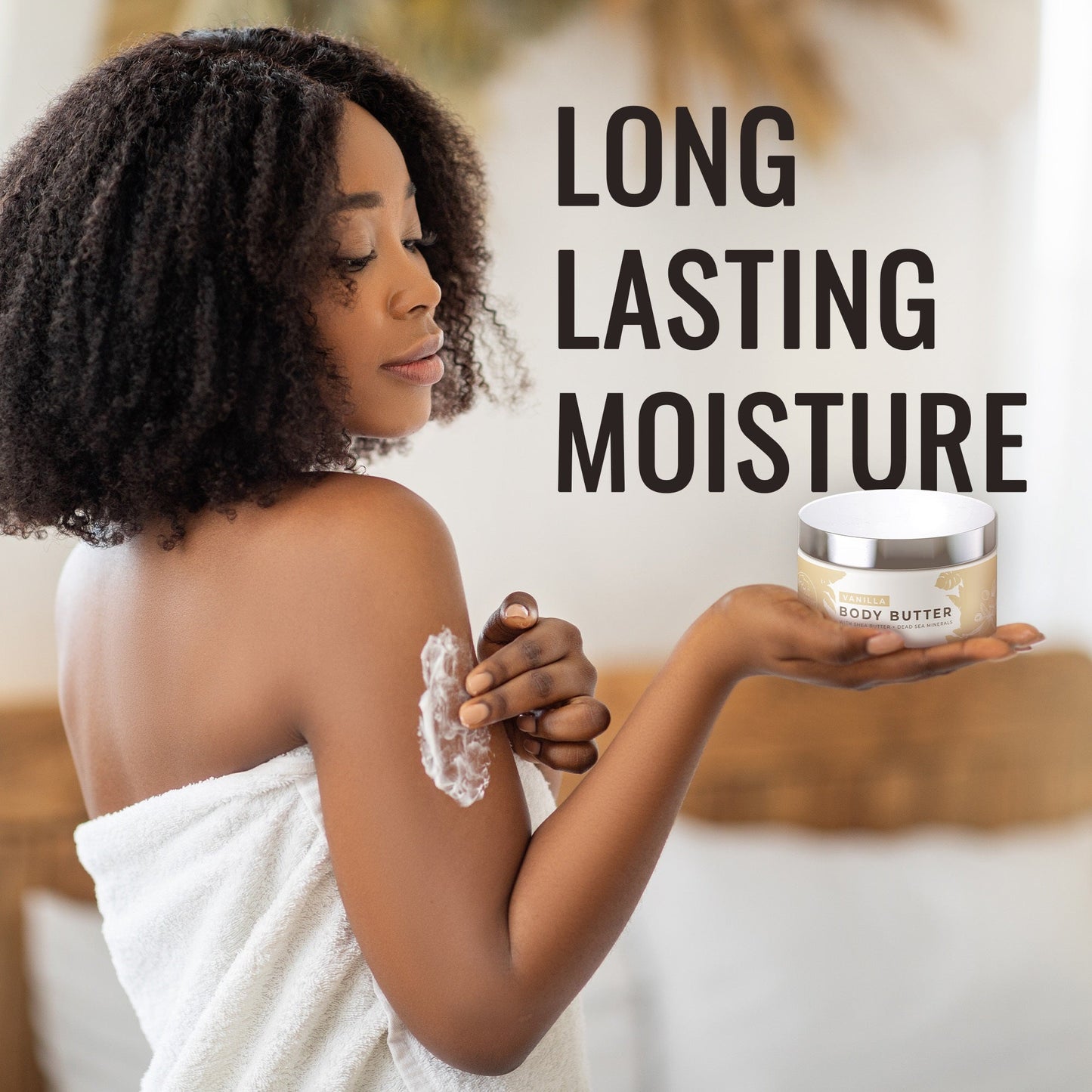 A woman in a towel applies Natural Elephant Dead Sea Shea Body Butter 9 oz with natural plant oils to her shoulder, holding the open jar. Beside her, text reads: LONG LASTING MOISTURE. The scene is bright and inviting.