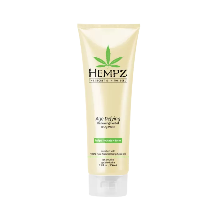 An 8.5 fl. oz. beige tube of Hempz Herbal Body Wash Age Defying Scent, featuring a green leaf logo and enriched with 100% pure vegan hemp seed oil, stands upright against a white background.