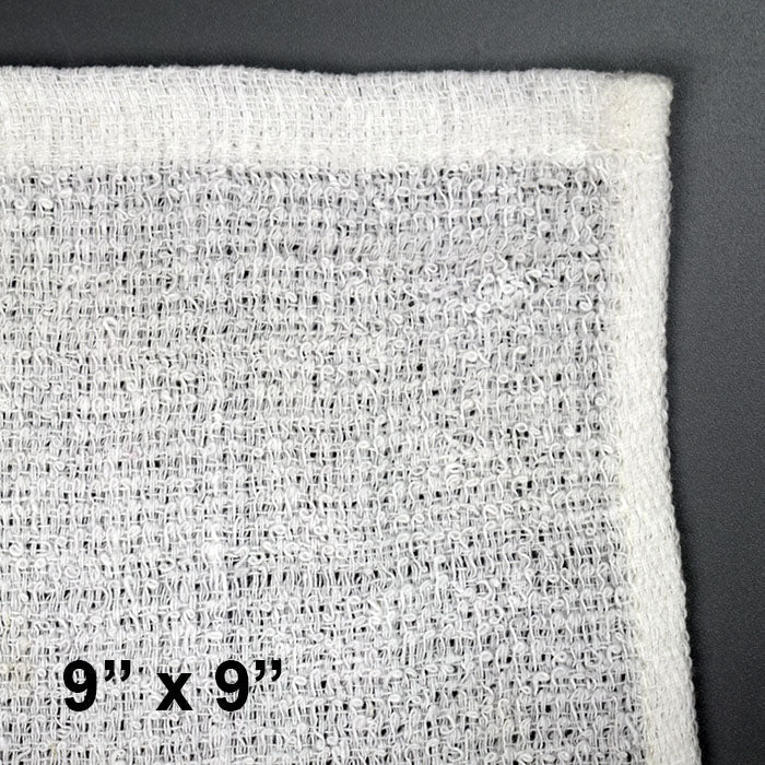 Close-up of a white, textured 100% cotton towel from the White Towel Services Starter Kit (9x9, 500ct) with stitched edges on a gray surface. The size is printed in black in the corner. Ideal for essential oils or use with the included deluxe warmer.