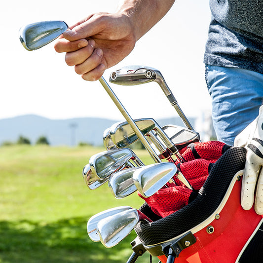 A golfer picks a club from a red golf bag on a scenic course, with White Towel Services Koala Kool Towel 250 ct. nearby for refreshment between swings.