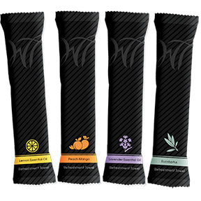 Four slim, black striped packets—each with a colorful lemon, peach-mango, lavender, or eucalyptus label—stand by plush 8x8 100% cotton towels from the White Towel Services Starter Kit with Deluxe Warmer for an aromatherapy experience.