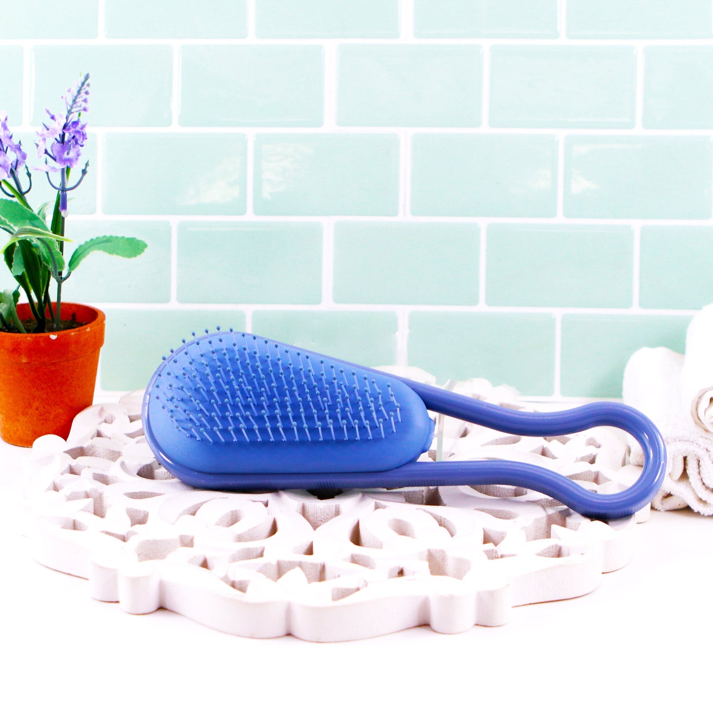 Wet Brush antimicrobial hair detangler brush in blue on a decorative mat with plants and towels