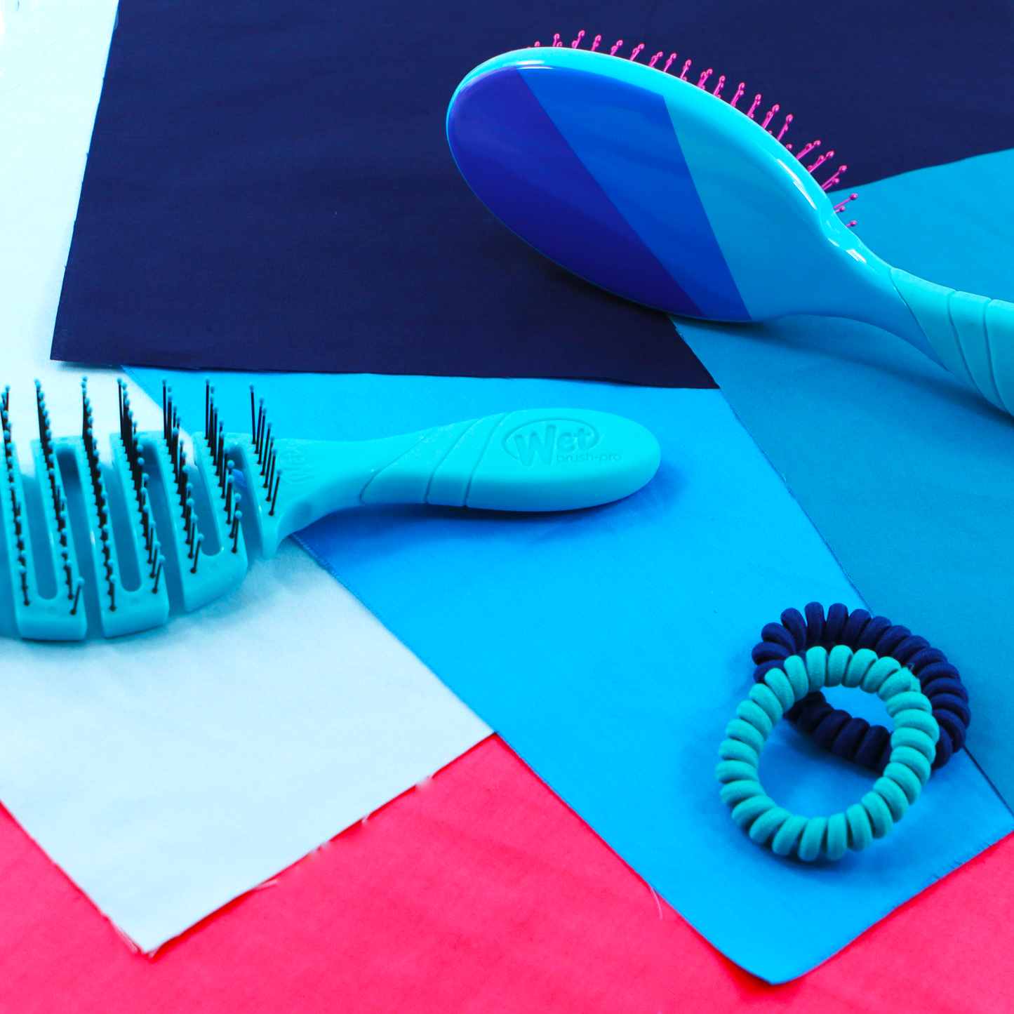 Wet Brush Color Me Happy Kit featuring two colorful detangling brushes and hair ties on vibrant fabric backgrounds