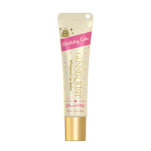 A tube of Glimmer Wish Whipped Lip Balm in Birthday Cake flavor, featuring sprinkles, gold text, a heart-shaped applicator cap, and nourishing organic butters for extra softness.