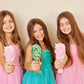 Three girls in colorful dresses holding unicorn detangling hair brushes with joyful expressions