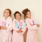 Three girls in pink robes happily holding unicorn conditioner for kids in colorful bottles