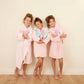 Three girls in pink robes holding bottles of unicorn shampoo for kids, smiling and enjoying bath time