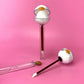 Glossy Pops Tropical Coconut Lip Balm in fun packaging with applicator and gloss tube on pink background