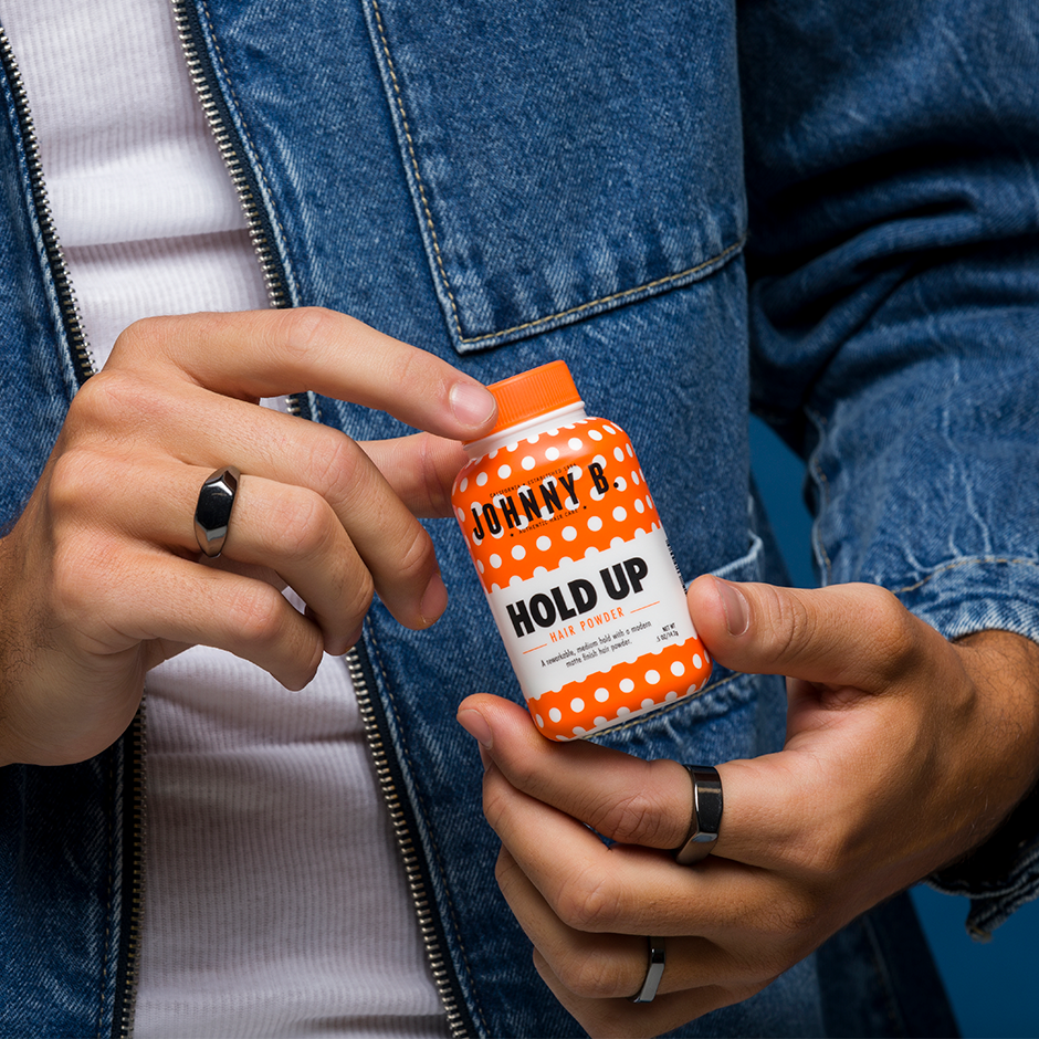 Johnny B Hold Up Hair Powder in an orange container with a person holding it stylishly