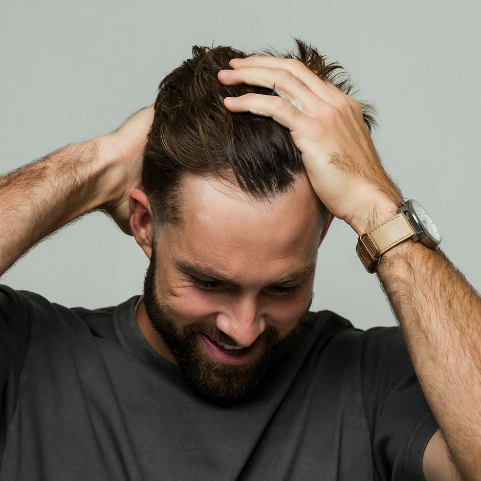 Man applying Johnny B leave-in conditioner to his hair for added moisture and control