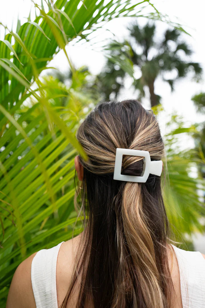 Medium white hair claw clip holding back a woman's hair among lush green foliage