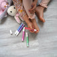Child using Piggy Paint pen polishes on toes while playing with plush toys on the floor