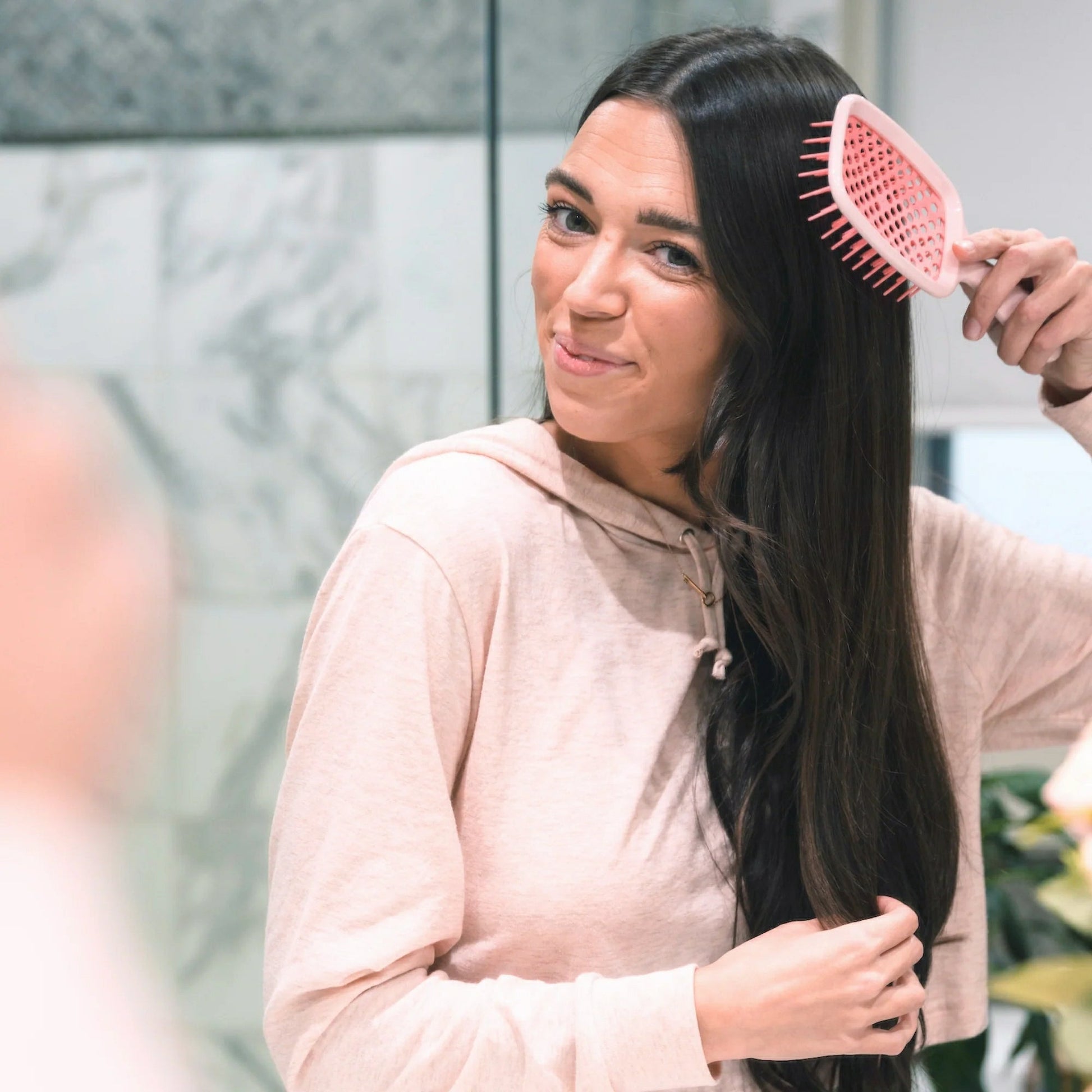 Unbrush detangling hair brush used by a woman for smooth, tangle-free hair in a modern bathroom
