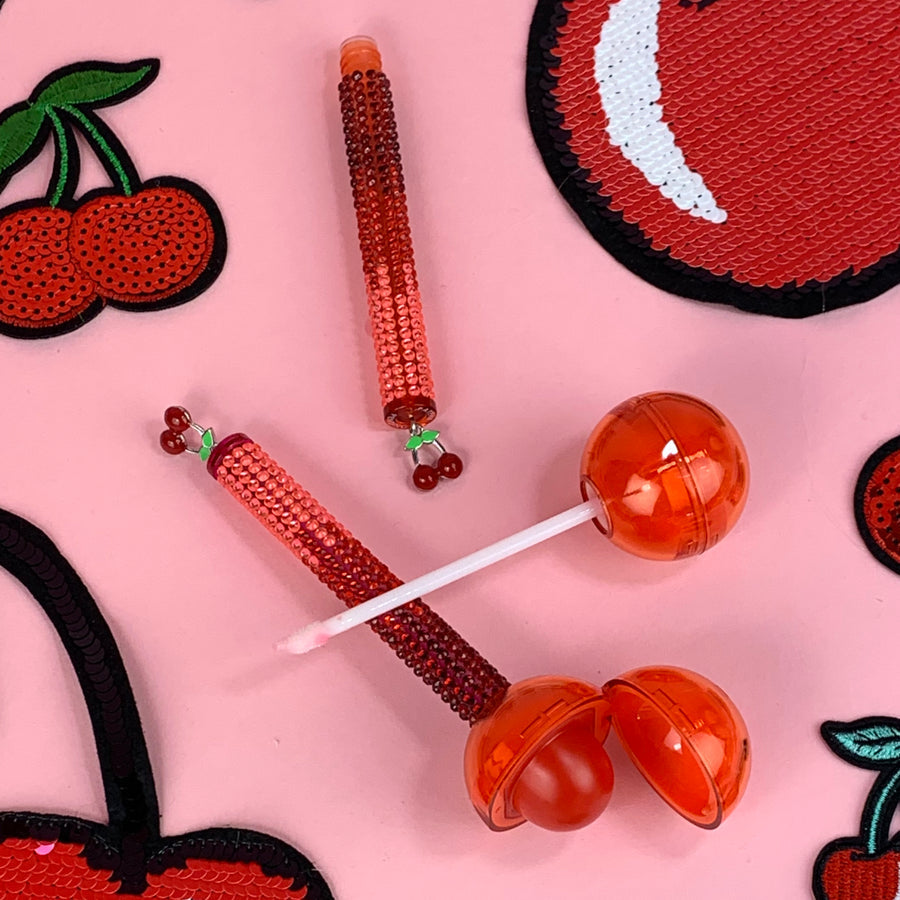 Glossy Pops TGI Fruity lip balm in cherry flavors with vibrant red packaging and fruity designs