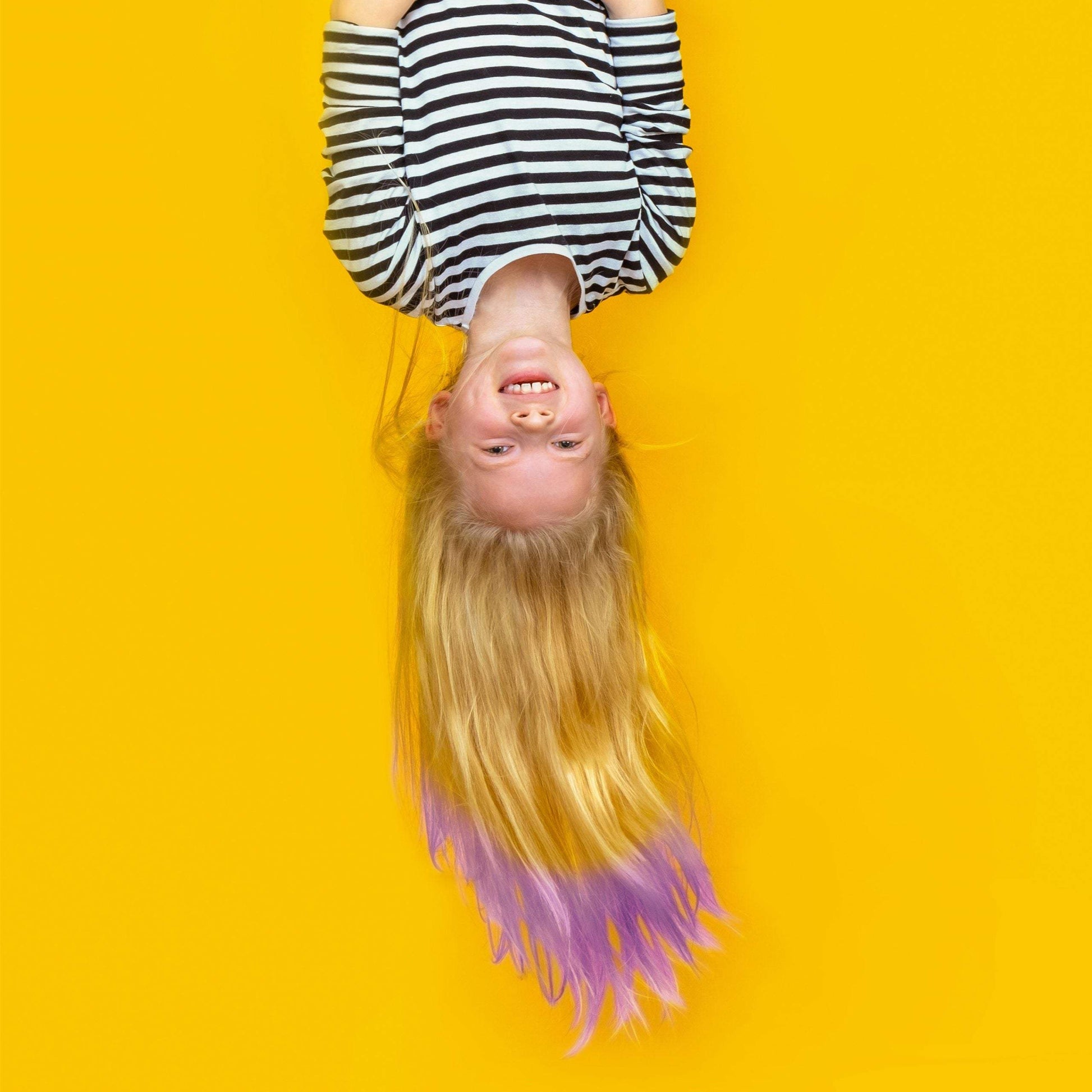 Girl with long blonde hair featuring purple hair color conditioner tips against a bright yellow background