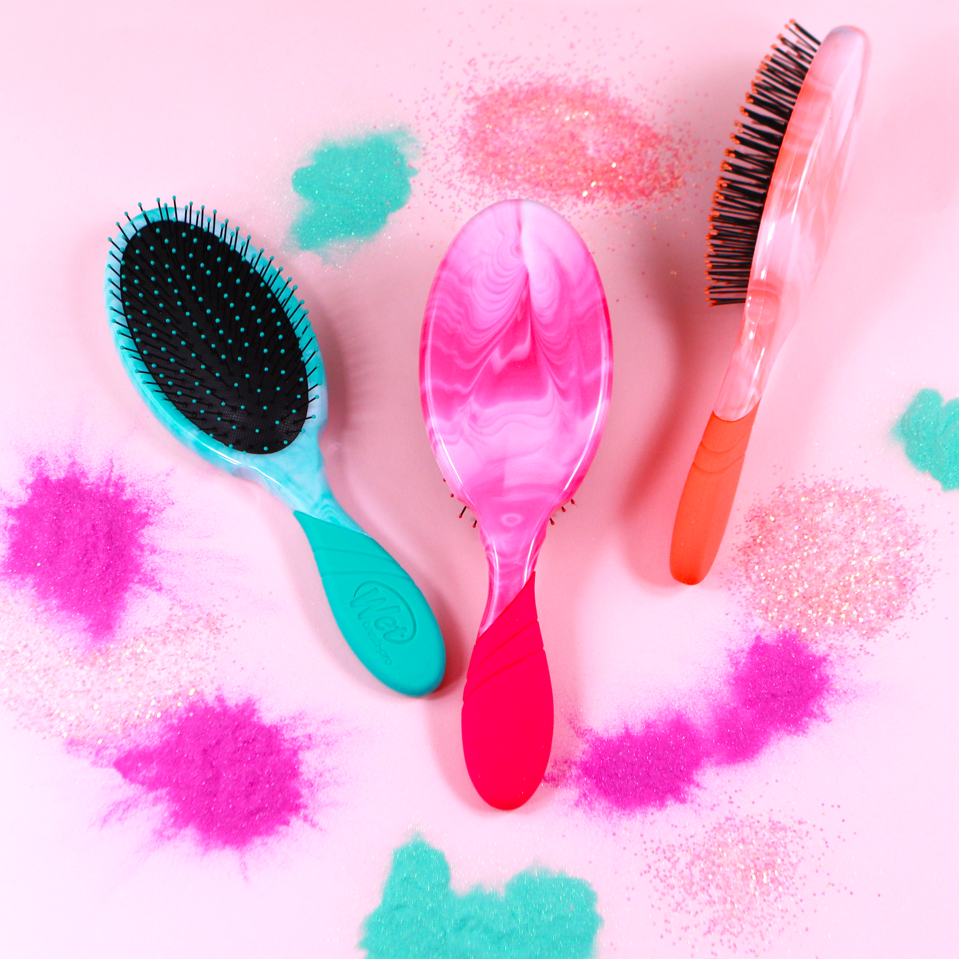 Three Wet Brush Color Shock detanglers in vibrant colors with a playful background of colorful glitter